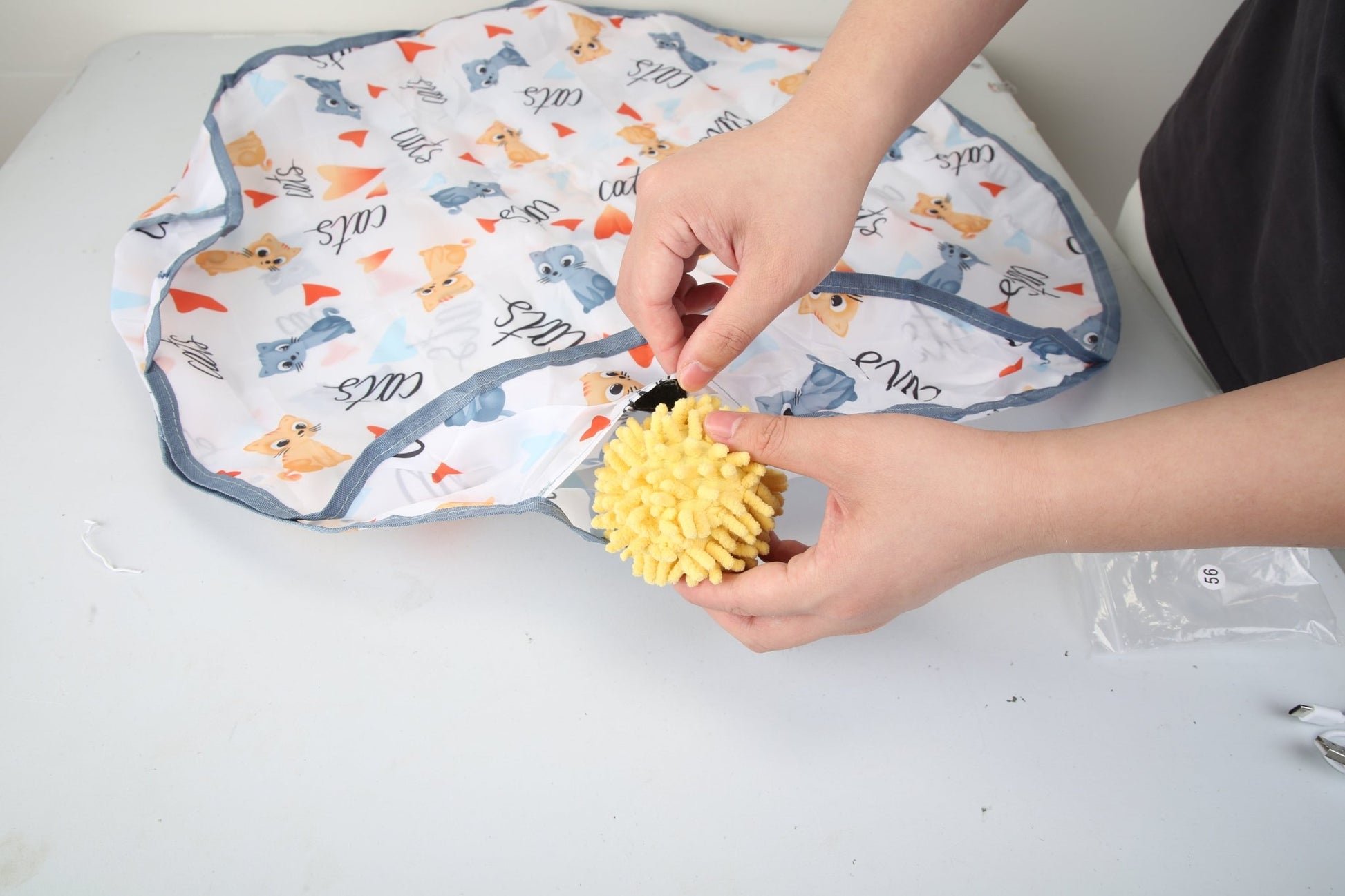 Interactive cat toy ball with textured yellow surface, shown with included hide-and-seek storage bag